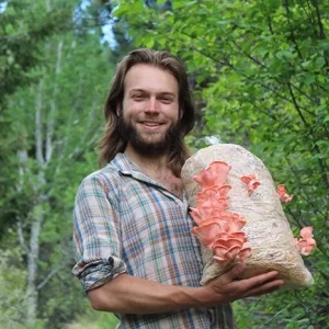 A bearded young man is holding a mushroom-growing bag