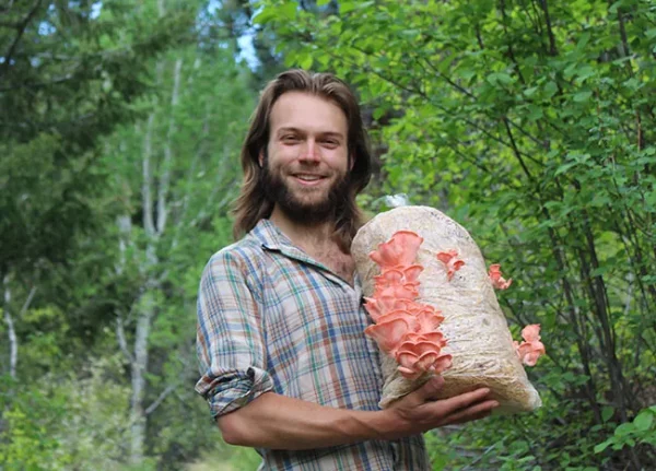 A bearded young man is holding a mushroom-growing bag
